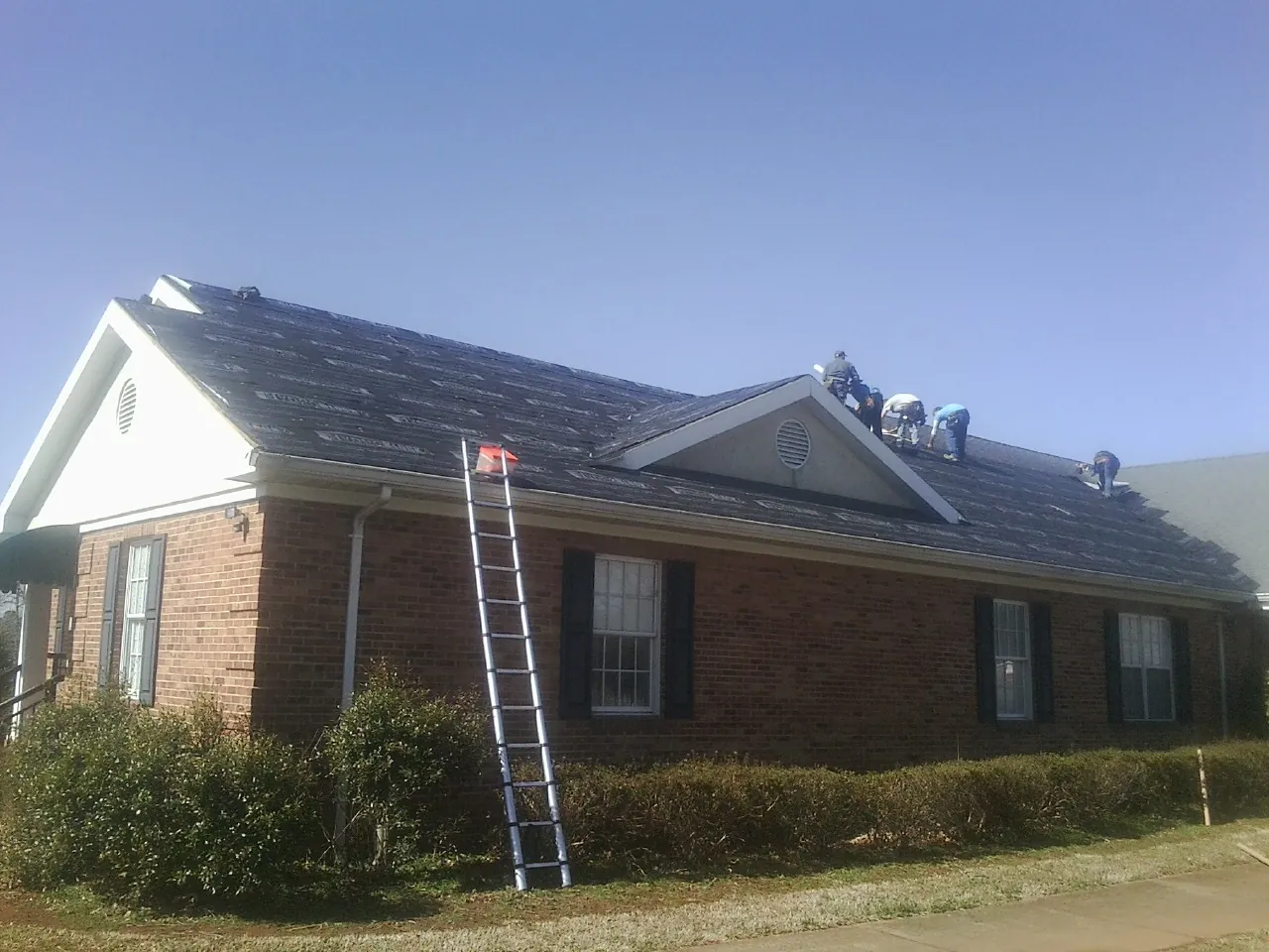 Crew tearing shingles off a brick ranch roof with a ladder set — Metal Roof Repair work by our crew in Coolidge